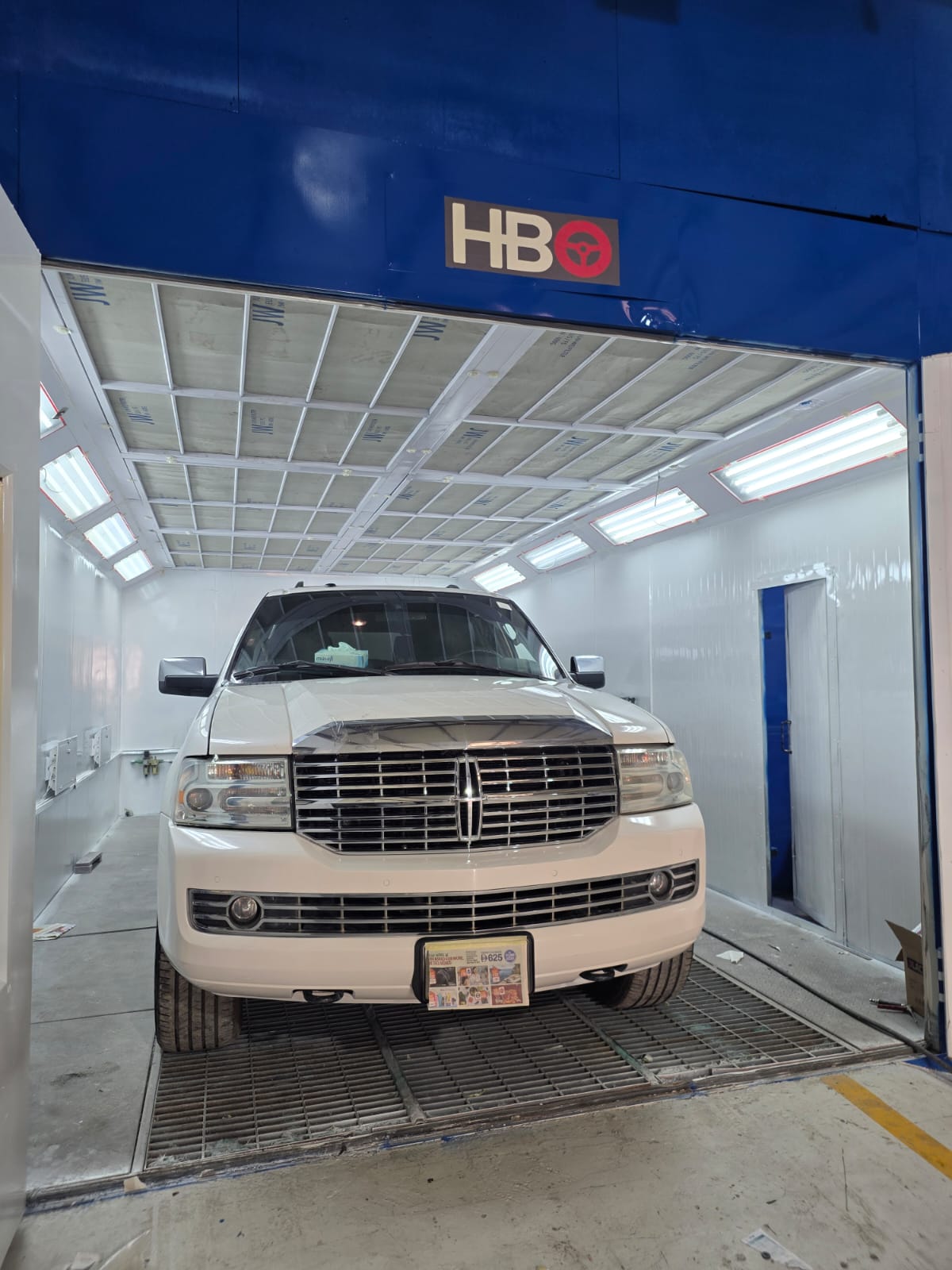White full-size SUV inside the paint booth, prepared ahead of painting
