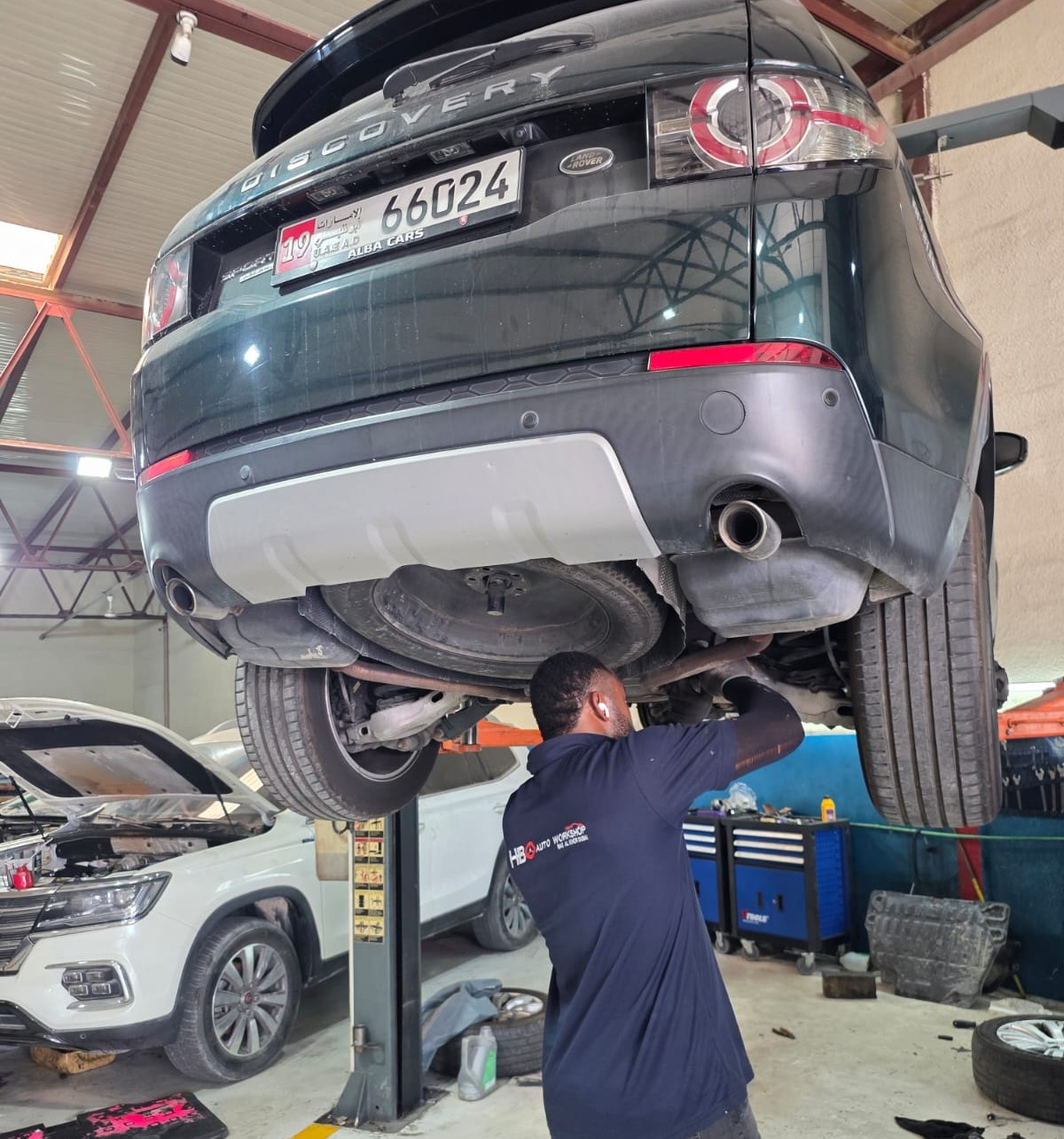 Technician in HBO uniform working underneath a Range Rover raised on a workshop lift