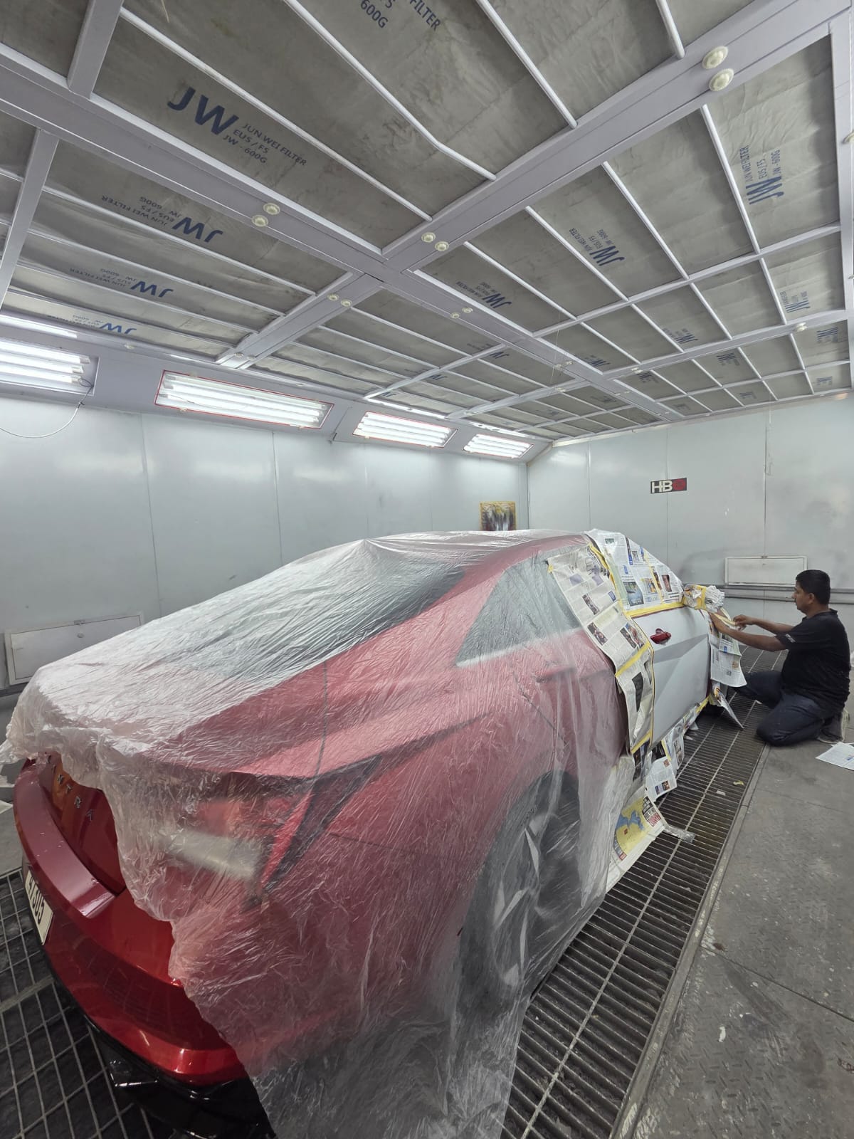 Red sedan masked and prepped for painting inside the paint booth