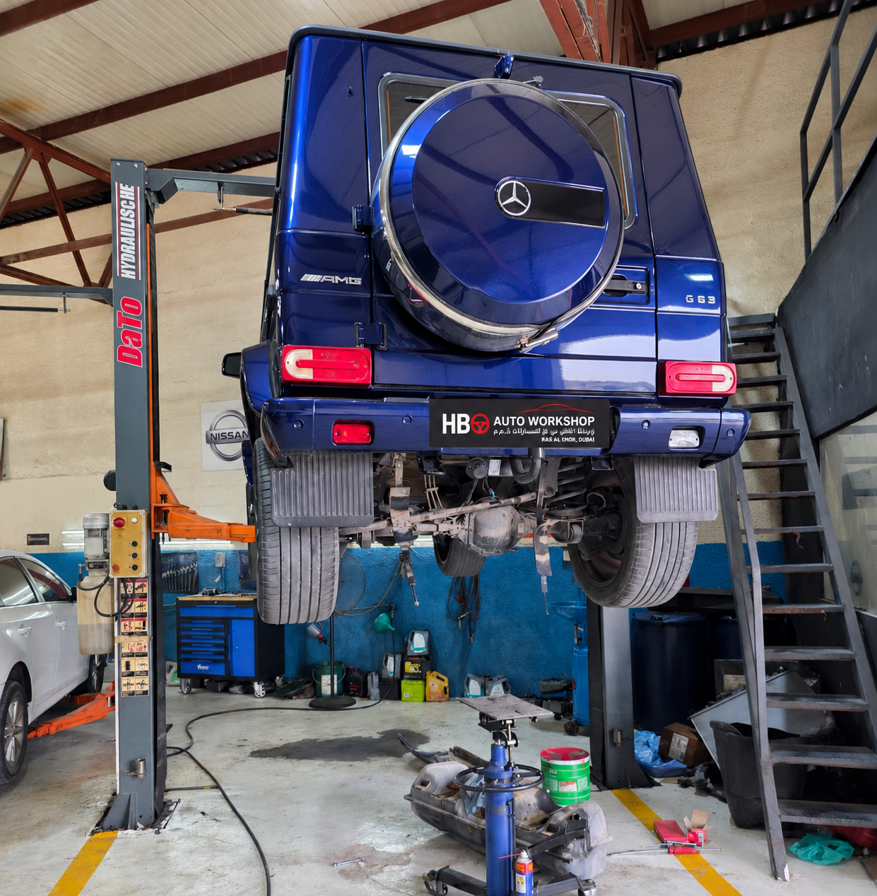 Blue Mercedes-Benz G 63 raised on a workshop lift with underbody parts removed