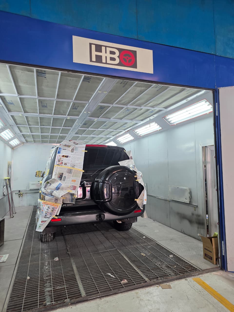 Dark-coloured SUV masked and prepped for painting inside the paint booth