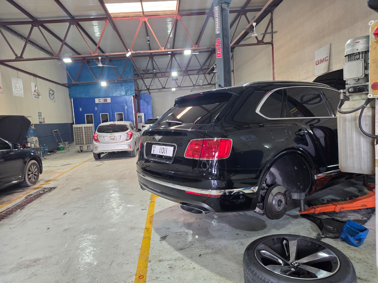 Black Bentley SUV with a rear wheel removed for brake work on a workshop ramp