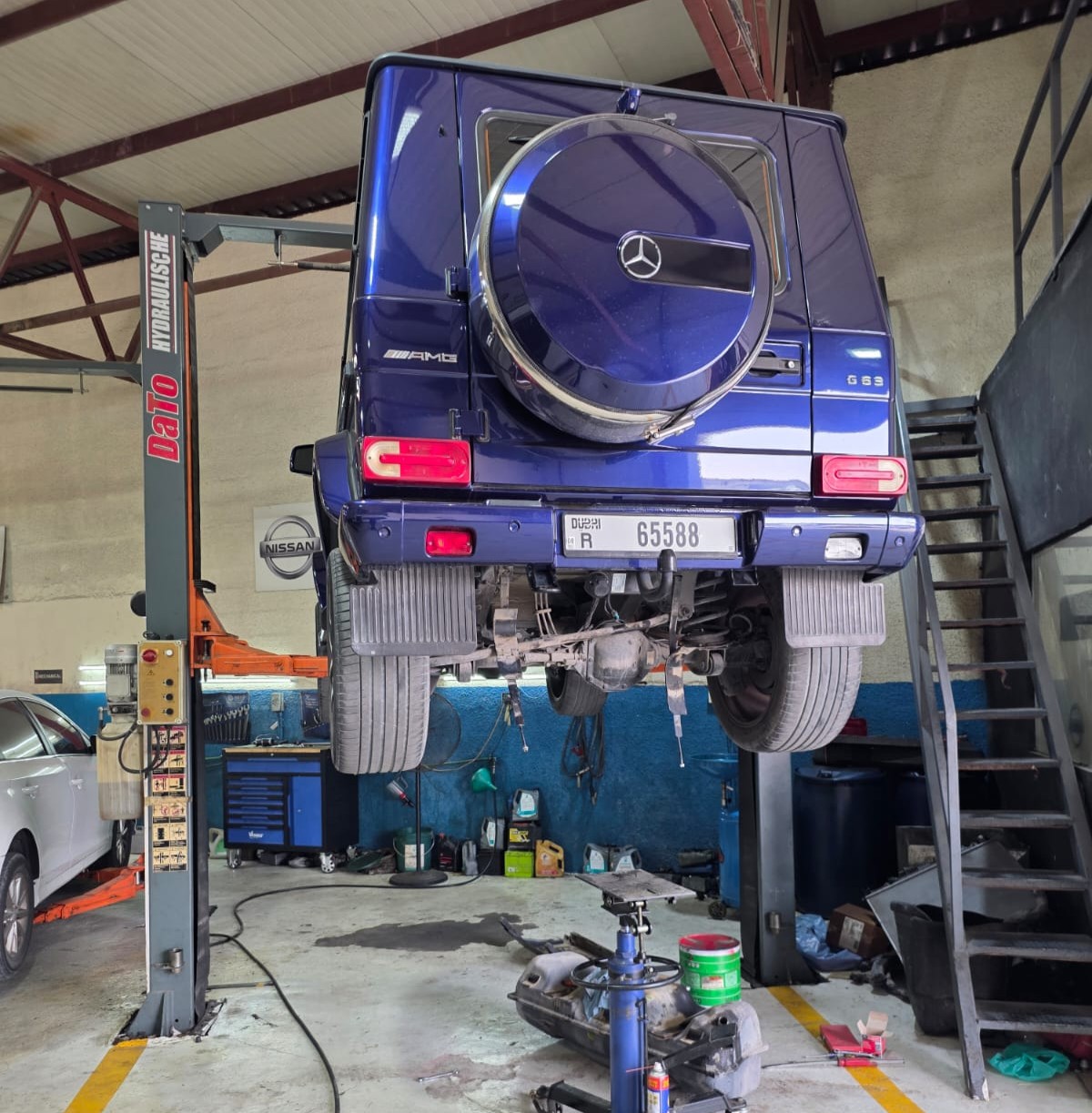 Blue Mercedes-AMG G 63 raised on a lift with the rear wheels removed for axle and suspension work