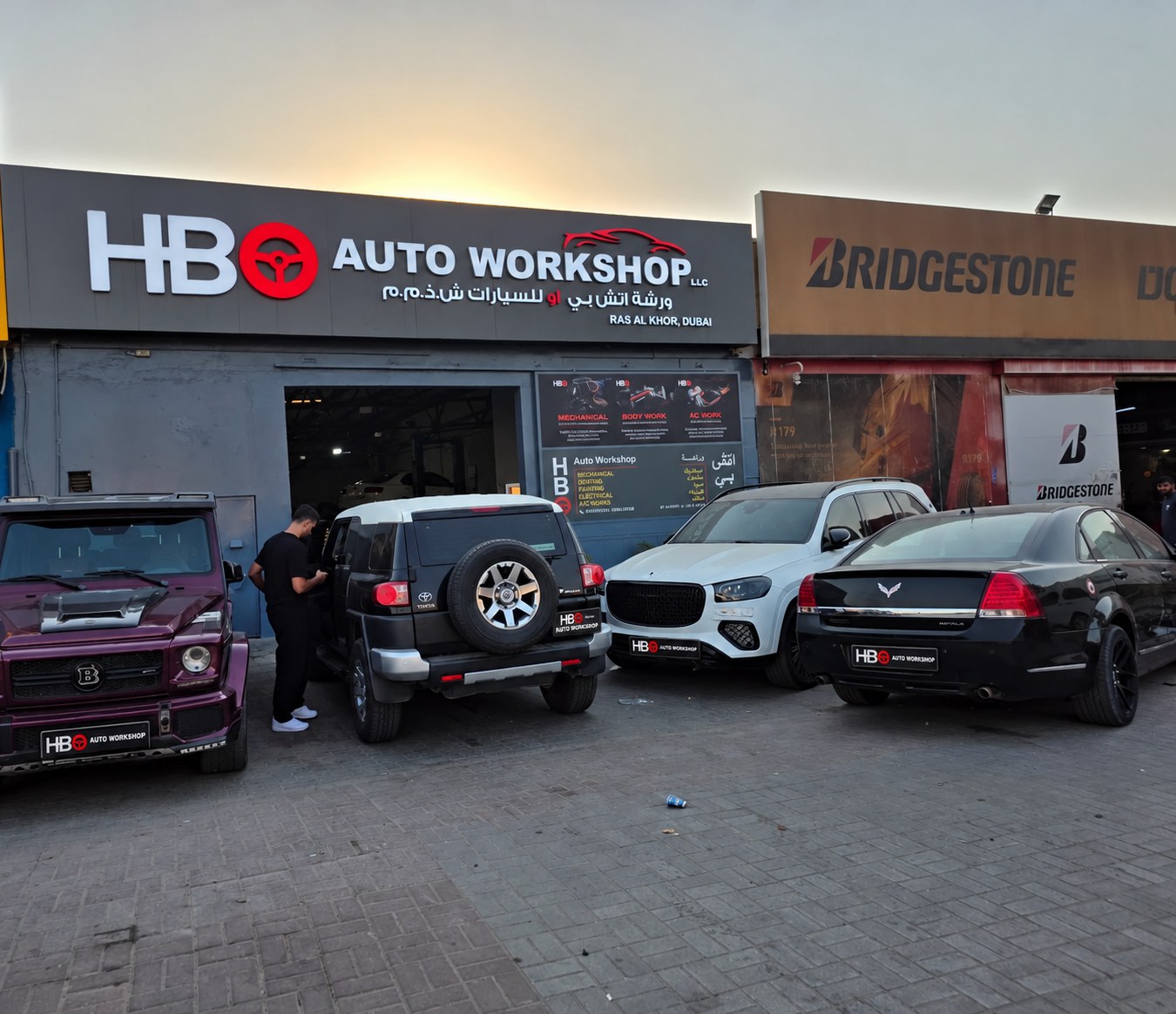 HBO Auto Workshop frontage in Ras Al Khor, Dubai, at sunset with cars parked in front of the workshop
